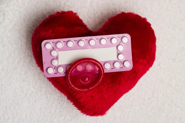Pillole contraccettive orali preservativo sul cuore rosso — Foto Stock