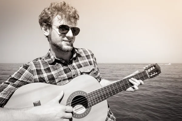 Giovane hipster suonare la chitarra dal mare oceano . — Foto Stock