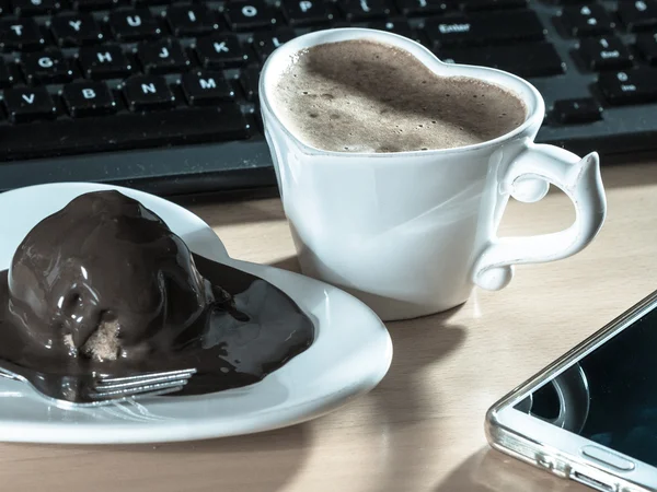 コンピューターの横にコーヒーとチョコレート ケーキのカップ. — ストック写真