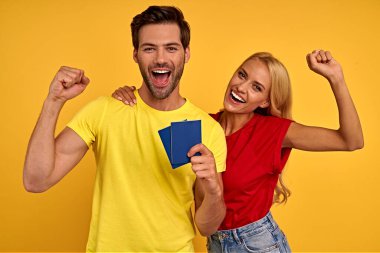 Sarı tişörtlü, gülümseyen iki arkadaş. Hafta sonları yurtdışına seyahat eden yolcular. Uçak yolculuğu konsepti. Pasaportlarınızı saklayın. Yaşasın bir yolculuğa çıkacağız..