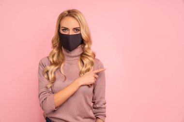 Pembe bluzlu genç bir kadın, koronavirüs virüsü virüsü Covid-19 'dan korunmak için steril yüz maskesi takıyor. Pandemik karantina sırasında, çalışma alanı üzerindeki parmakları işaret ediyor.