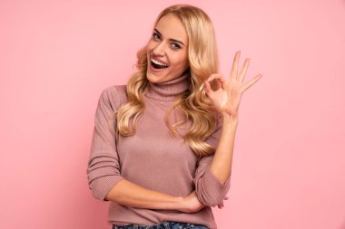 Pembe arka planda izole bir şekilde duran mutlu genç kadın görüntüsü iyi bir jest gösteriyor. Kameraya bak