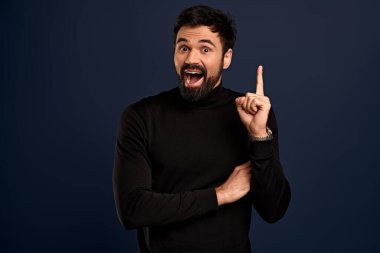 Got excellent idea. Creative good-looking bearded man, raise one finger and smiling astonished as have something say, give good suggestion during meeting with coworkers,Pacific Blue background.