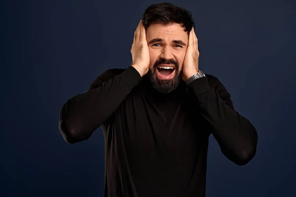 Shocked concerned young man stare speechless and distressed at camera, grab head with both hands and gasping, look worried and concerned as facing difficulties, standing troubled Blue background.