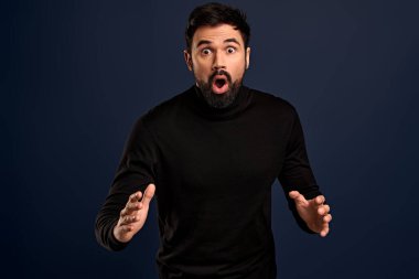 Şaşırmış bir adamın kötü haberi duyunca dehşete kapılan ve panikleyen, mavi beton arka planda izole edilmiş şaşırmış görüntüsü. Duygusal merakı olan genç bir erkek şaşkınlık içinde..