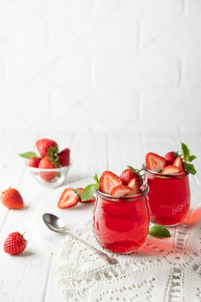 Sweet dessert jelly pudding with strawberries in glass jar on white background