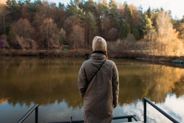 Gölün kenarında duran montlu genç kadın.