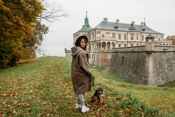 秋に古城の近くを犬が歩いている若い女性が — ストック写真