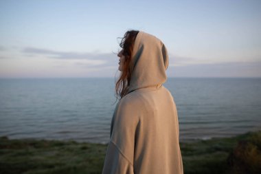 Akşam denizinin arka planında, dağda duran genç bir kadın.