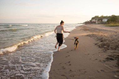 Deniz kenarında eğlenen av köpeği olan genç bir kadın.