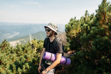 Sırt çantası ve dağın tepesinde bir paspas olan genç bir adam.