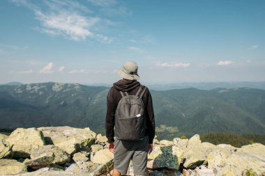 Sırt çantalı genç bir adam bir dağın tepesinde duruyor.