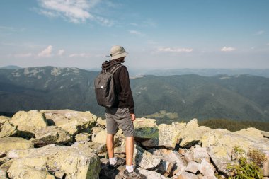 Sırt çantalı genç bir adam bir dağın tepesinde duruyor.