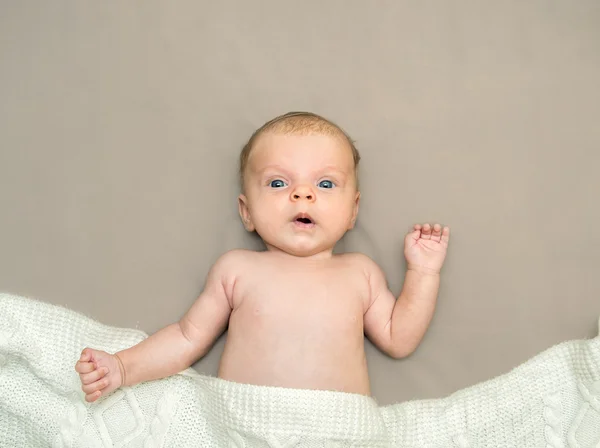 Verbaasd babymeisje met blauwe ogen, liggend op een deken. — Stockfoto