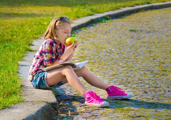 Bir elma yemek sokakta oturan küçük kız. — Stok fotoğraf