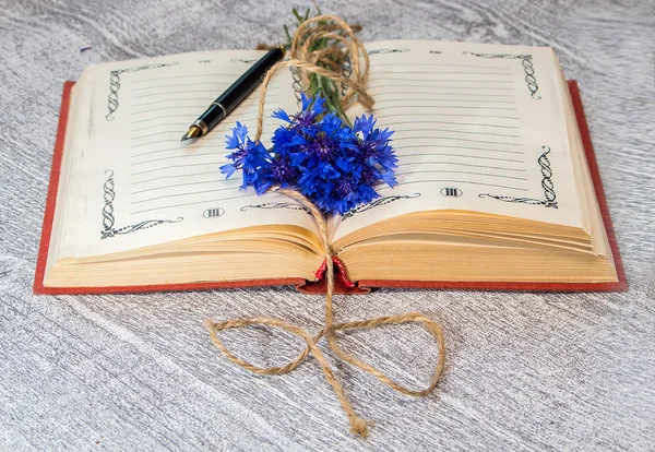 Aufgeschlagenes Buch mit einem Bund blauer Kornblumen — Stockfoto