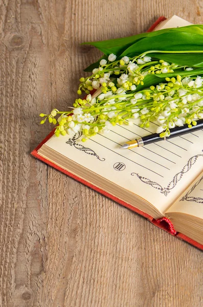 Цветы долины на книге для записей и ручки — стоковое фото