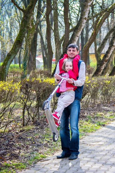 Pai e filha em uma scooter em um parque em um passeio — Fotografia de Stock