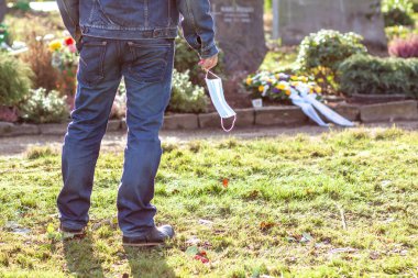Salgın sırasında maske takmış aile üyelerinin mezarında dikilen bir adam.