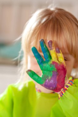 Salgın sırasında evde suluboya boyasının arkasına saklanan küçük bir kız.