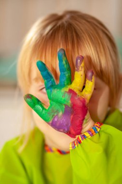 Salgın sırasında evde suluboya boyasının arkasına saklanan küçük bir kız.