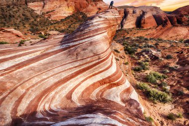Tanımlanamayan yürüyüşçü, Nevada, ABD 'deki Fire State Park Vadisi' ndeki Wave Rock 'tan gün batımını izliyor.