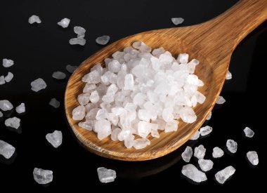 Siyah arka planda deniz tuzu kristalleri olan tahta kaşığın en üst görüntüsü.