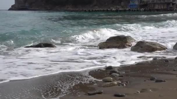 Una piccola onda di puro Mar Nero corre su una pietra sulla spiaggia sabbiosa deserta del villaggio di Novy Svet in Crimea. Giornata nuvolosa all'inizio della primavera — Video Stock