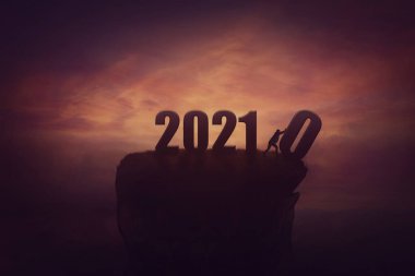 Silhouette of a determined man on the top of a cliff over sunset, announcing the new 2021 year coming, and throws out in the abyss the old 2020. Surreal seasonal scene, change concept and time control clipart
