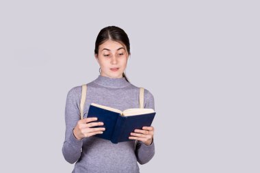 Sersemlemiş, duygusal genç bir kadın bir kitaba hayran bakıyor, şok edici bir mesaj buldu. Şaşırmış öğrenci kız okuyucu elinde kırmızı bir ders kitabı tutuyor beyaz duvarın üzerinde kopya alanı ile izole edilmiş.