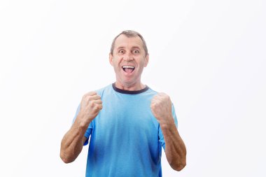 Memnun orta yaşlı adam yumruklarını sıkıca havada tutar, kameraya olumlu duygularla bakar, beyaz arka planda izole olur. Minnettar orta yaşlı adam başarıyı kutluyor..