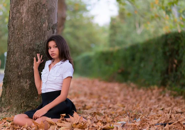 Bella ragazza seduta sulle foglie d'autunno — Foto Stock