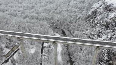 Kışın dağdaki nehrin üzerinden geçen otobanın hava aracı görüntüsü.