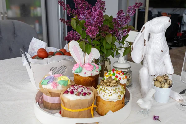 Ostern. Osterkuchen, Flieder, Hase, bemalte Eier, Urlaub, Esstisch mit weißer Tischdecke Stockbild