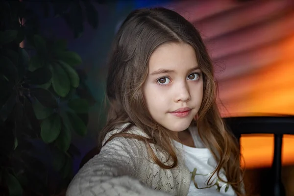 Schattig wit tienermeisje met lang golvend haar zit bij het raam aan een tafel binnen met houten muren en denkt aan iets, glimlacht — Stockfoto