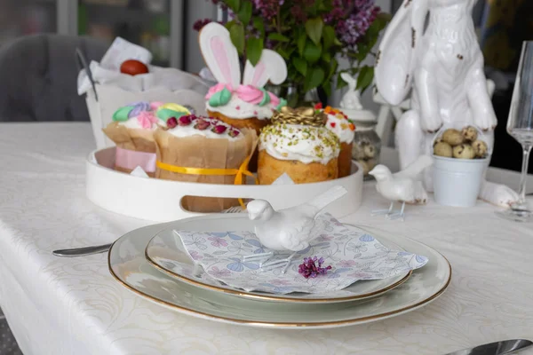 Ostern. Osterkuchen, Flieder, Hase, bemalte Eier, Urlaub, Esstisch mit weißer Tischdecke Stockfoto