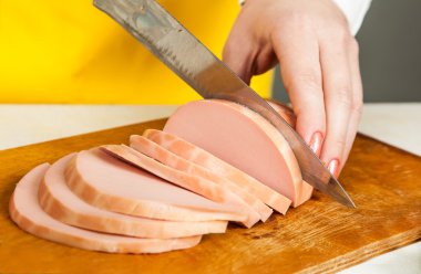 kadın bir bıçak sosis dilimleri kesiyor. 