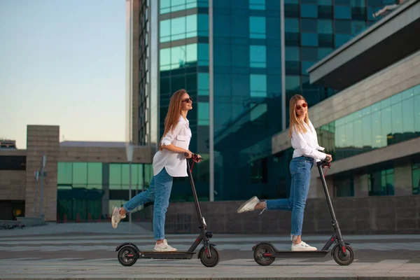 Beautiful young women is enjoying sunny summer day while riding around the city on electro kick scooters. Lifestyle. — Stock Photo, Image