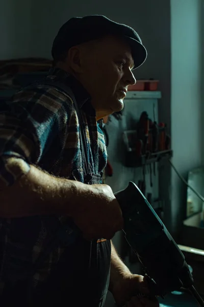 Älterer Mann mit Hammer arbeitet in Werkstatt Stockbild
