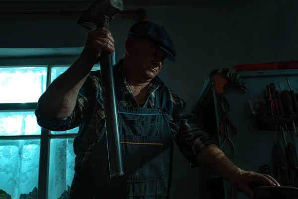 Älterer Mann mit Hammer arbeitet in Werkstatt Stockfoto