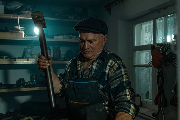 Elderly man with a hammer works in a workshop Stock Picture