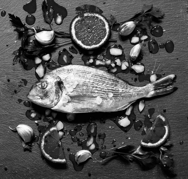 Orata de peixe fresco sobre uma pedra preta com legumes — Fotografia de Stock