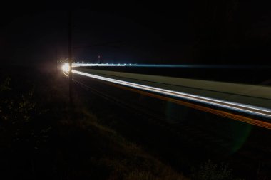 Train front light colorful trails on rails. Travel at night, long exposure