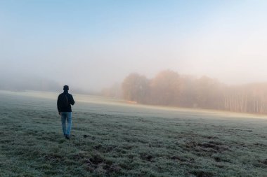 Genç adam sonbahar ormanıyla çayırda yürüyor dondurucu sisli bir sabahta. Çek manzarası