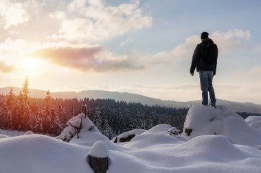 Gün batımında sırt çantasıyla kar kayasının üzerinde duran genç adam. Novohradske Dağı, Çek Cumhuriyeti