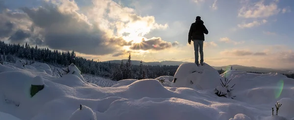 Panoramic view young man from back standing on snow rock with backpack at sunset. Novohradske mountain, Czech republic