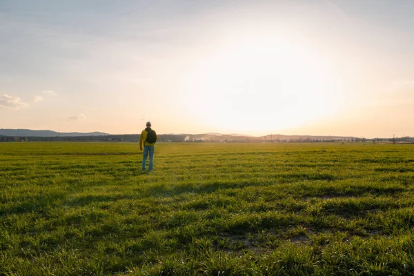 穿着黄色夹克 背包的年轻高加索人男子站在草地上 黄昏时分站在山溪春景的田野里 — 图库照片