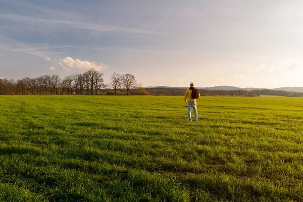 穿着黄色夹克 背包的年轻高加索人男子站在草地上 黄昏时分站在山溪春景的田野里 — 图库照片