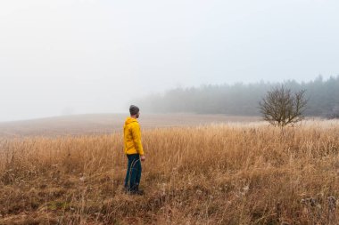 Sarı ceketli adam kışın Çek topraklarında sisle yürüyor. Yan görünüm
