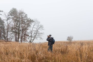 Ceketli ve pantolonlu bir adam kış sisi manzarasında fotoğraf çekiyor. Hobi geçmişi